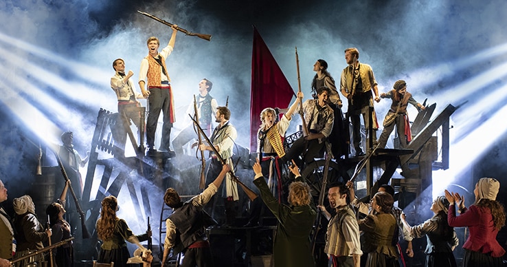 The chorus of Les Miserables sings from atop the barricade.