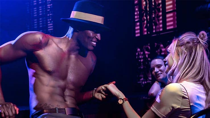 A smiling dancer from Magic Mike Live takes the hand of an audience member.