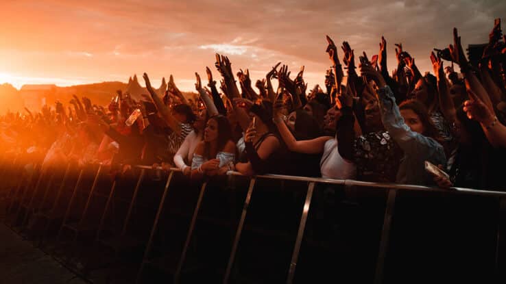 A crowd celebrates at a music festival as the sun sets