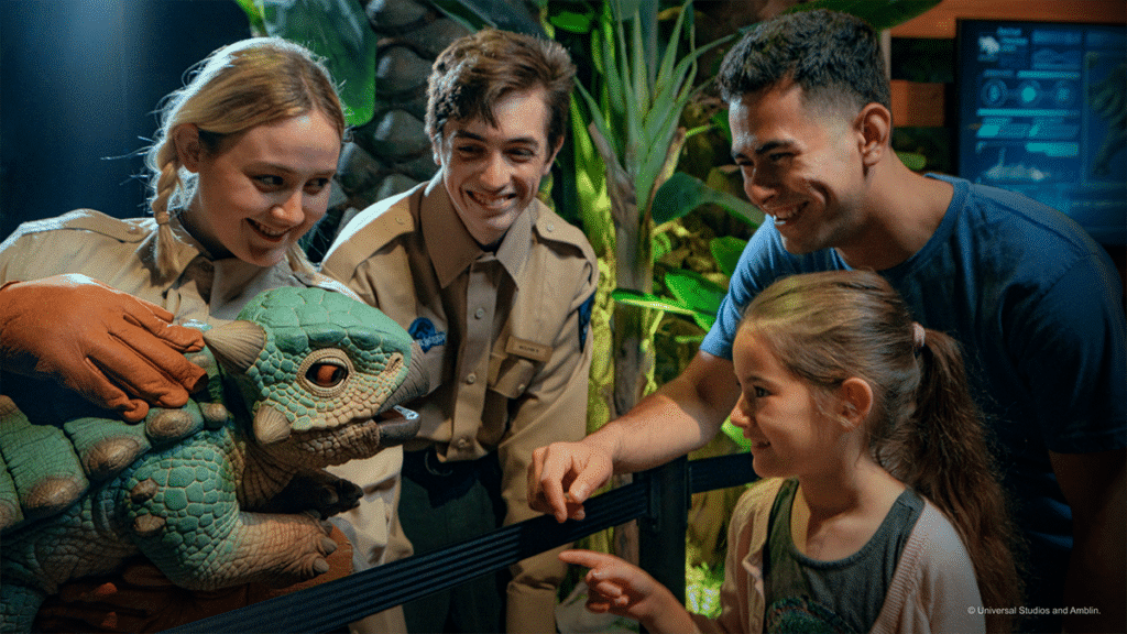 Two park wardens at Jurassic World: The Experience, in Manchester, hold Bumpy the dinosaur for a man and child to see up close