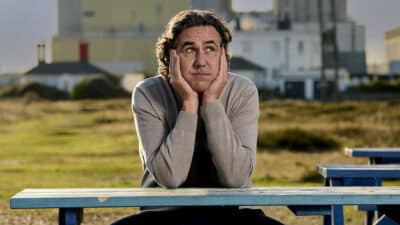 Micky Flanagan sits at a picnic table, looking morose