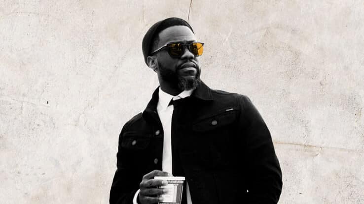 Kevin Hart wears a pair of sunglasses, holding a cup of coffee