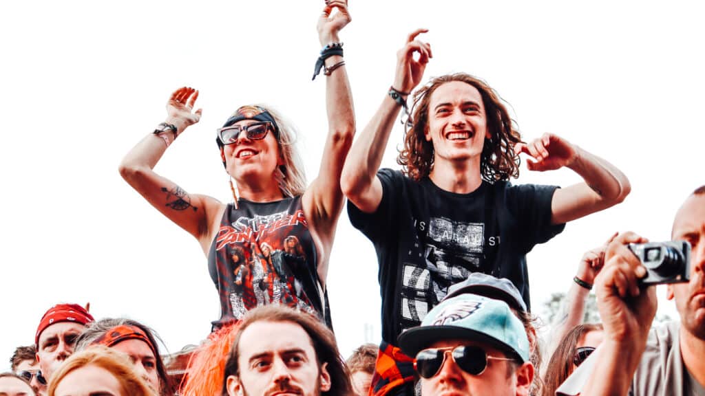 A couple in a festival crowd sit atop a sea of shoulders