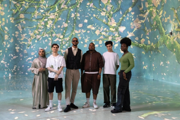 A group of poets stand in front of a digital painting at FRAMELESS