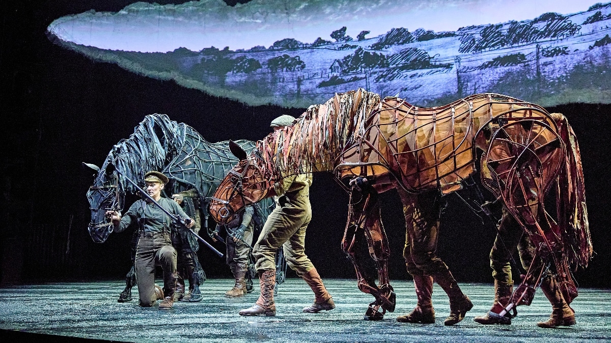 Actors dressed in military uniform guide life sized horse puppets in the West End production of War Horse