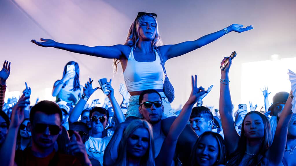 A girl holds her arms wide atop someone's shoulders in the crowd at Creamfields