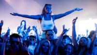 A girl holds her arms wide atop someone's shoulders in the crowd at Creamfields