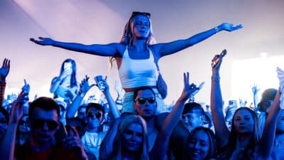 A girl holds her arms wide atop someone's shoulders in the crowd at Creamfields