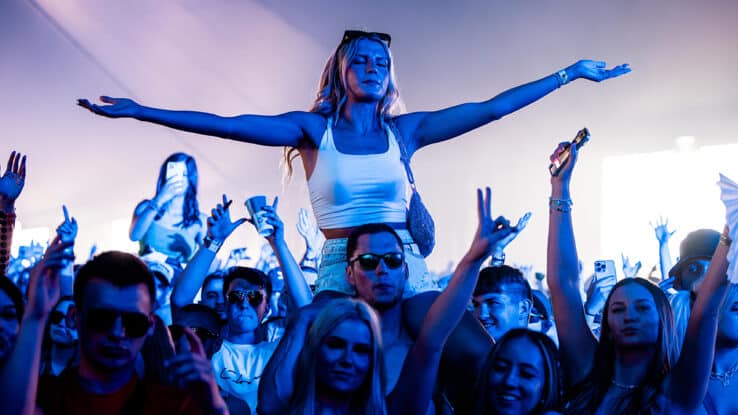 A girl holds her arms wide atop someone's shoulders in the crowd at Creamfields