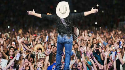 Garth Brooks stands on a stage before a sea of fans, spreading his arms wide