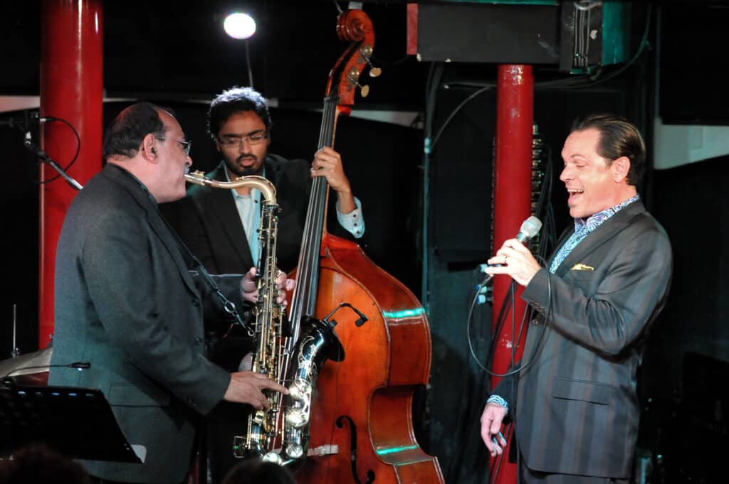 A singer, a saxophonist and a double bass player perform onstage during a jazz festival