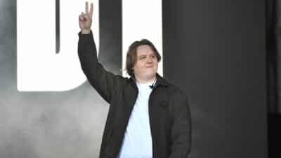 Lewis Capaldi holds up two fingers in a peace sign on stage