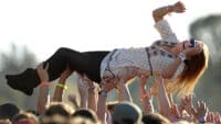 A festival goer crowd surfs over an audience of outstretched arms