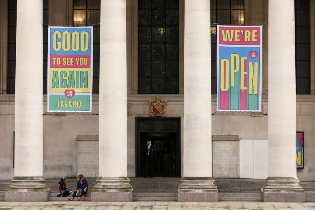 Banners reading 'Good To See You Again (Again)' and 'We're Open' are seen as Manchester Central Library