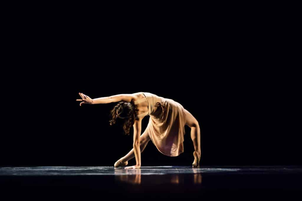 Teenager girl performing ballet dance on dark stage