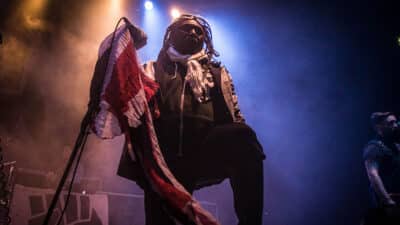 Benji Webbe of Skindred Performs on stage holding a tattered Union Jack flag