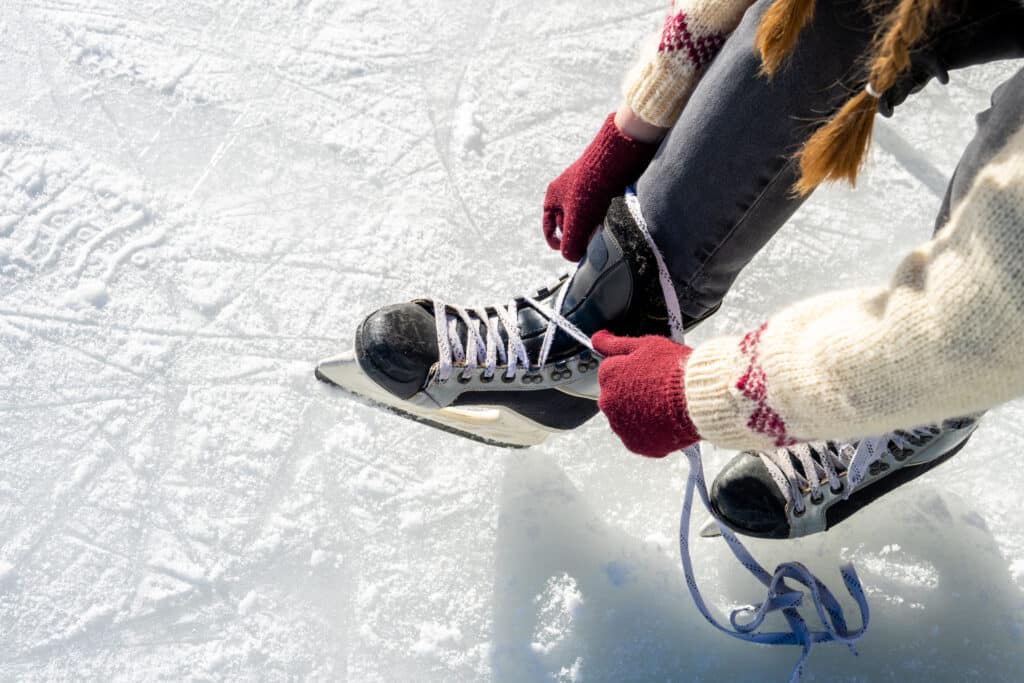 Woman tying ice skate shoelaces close view on frozen lake in natural parkland in winter