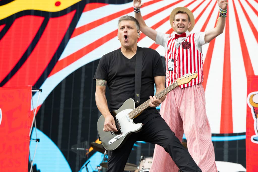 Singer Chris DeMakes of Less Than Jake performing live on stage while a backing performer jumps behind him