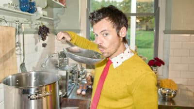 Harry Styles, blowing on a giant spoon to cool the contents, as he stands over a cooking stove