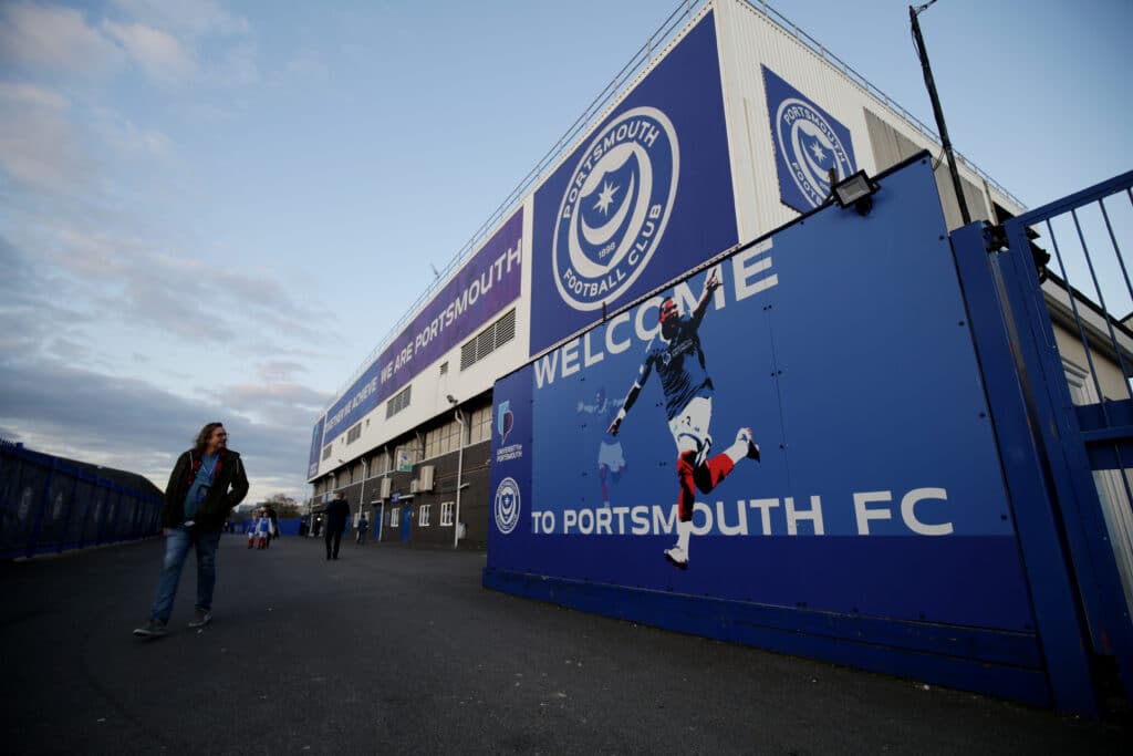 The exterior of Fratton Park football club, with a Portsmouth Football Club fan walking past