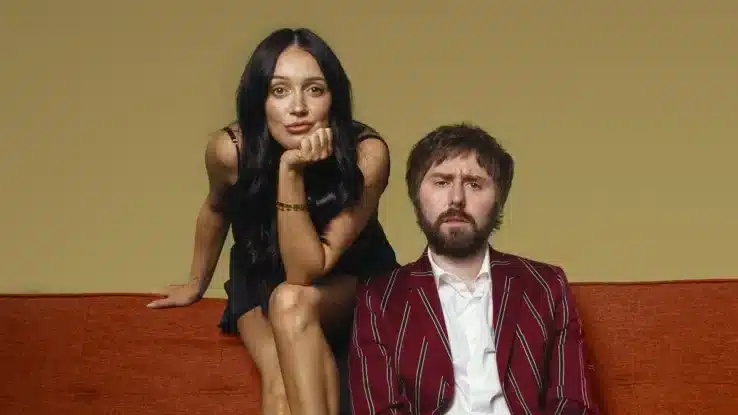 Clair Buckley and James Buckley sit on a sofa, looking bored.