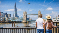 Two tourists standing on a bridge and looking at London landmarks