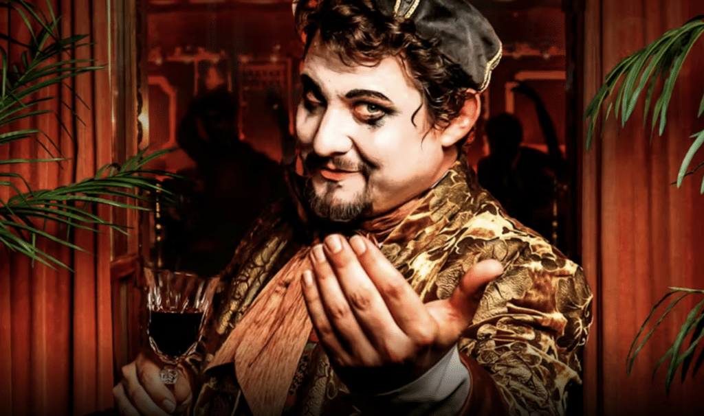 A man wearing 1830s clothing and holding a small glass gesturing to enter