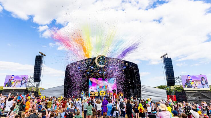 Rainbow confetti bursts over the crowd at the main stage of Camp Bestival
